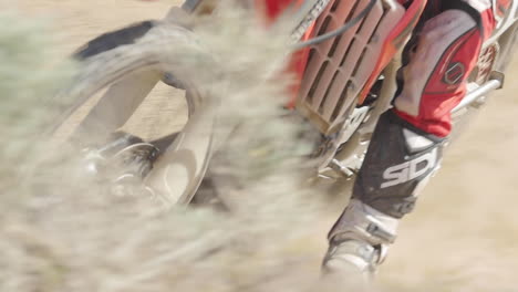 SLOW-MOTION:-A-dirt-biker-rides-his-red-motorcycle-through-the-desert-and-whips-around-a-berm