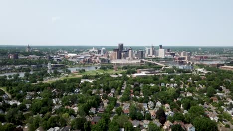 Amplia-Toma-Aérea-Avanzando-Y-Bajando-Lentamente-Con-La-Ciudad-De-Saint-Paul,-Minnesota-En-El-Horizonte-Junto-Al-Río-Mississippi-Rodeada-De-árboles-Y-Casas-En-Un-Día-Soleado