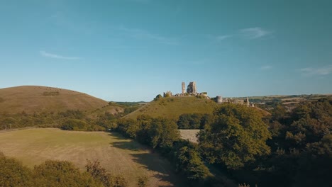 Drone-Volando-Sobre-Las-Ruinas-Del-Castillo-En-Una-Montaña-Verde-Al-Atardecer,-Inglaterra,-Reino-Unido