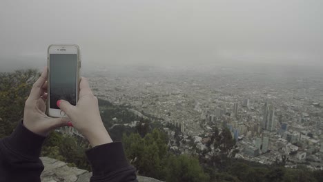 Woman's-hands-taking-a-panoramic-image-of-the-downtown-area-of-Bogotá,-Colombia-from-the-hills-in-Monserrate-with-her-smartphone