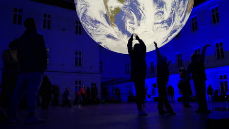 Kinder-Fotografieren-Und-Tanzen-Vor-Einem-Surreal-Wirkenden-Planeten-Erde,-Der-Sich-In-Einem-Universitätsgebäude-Dreht