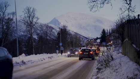 Static-shot-of-cars-driving-on-snowy-road-with-giant-snow-covered-mountains-in-background