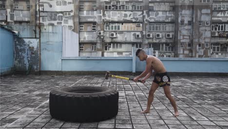 Un-Hombre-Hace-Ejercicio-En-La-Azotea-De-Un-Edificio-Mientras-Golpea-Un-Neumático-De-Gran-Tamaño-Con-Un-Martillo-Pesado-En-Hong-Kong.