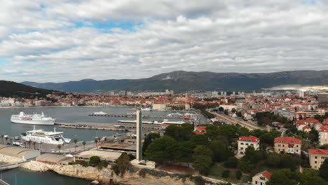 Die-Drohne-Steigt-Langsam-Auf,-Während-Sie-Sich-Dreht,-Um-Die-Wunderschöne-Stadt-Split-Und-Die-Fähren-Im-Hafen-Mit-Dramatischen-Wolken-Im-Hintergrund-Zu-Enthüllen