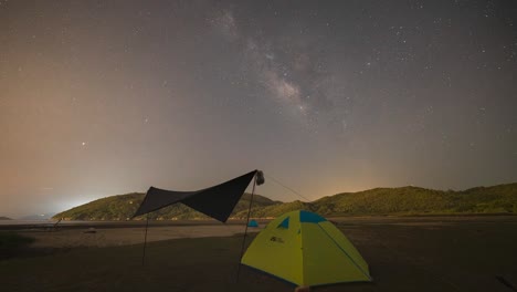 yellow-tent-under-Milky-Way-Galaxy-Time-Lapse-Lantau-Island,-Hong-Kong,-Universe-galaxy-milky-way-time-lapse,-dark-galaxy-view,-star-lines,-traffic-lights-timelapse-night-sky-stars-on-sky-background