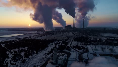 Eine-Drohne-Fliegt-Durch-Rauch-Und-Dampf-Und-Enthüllt-Das-Sherco-Kraftwerk,-Während-Im-Hintergrund-Die-Sonne-Untergeht