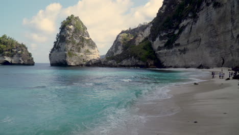 Las-Olas-Rompen-En-La-Orilla-De-Diamond-Beach-En-Nusa-Penida-Con-Un-Grupo-No-Identificado-De-Personas-En-El-Fondo.