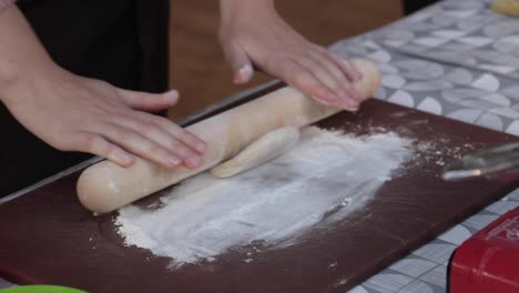 Mujer-Extendiendo-Masa-Con-Un-Rodillo-De-Madera-Sobre-Una-Cama-De-Harina,-Preparando-Comida