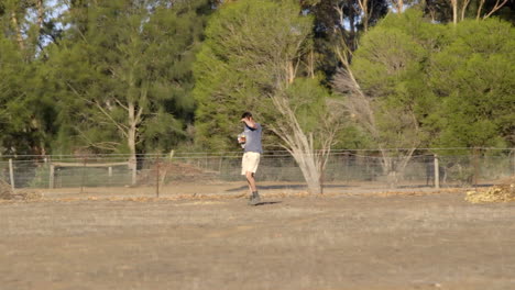 A-man-or-farmer-walking-through-a-farm-field-or-paddock-on-a-hot-summers-day-looking-towards-the-sun-in-the-paddock-for-the-farm-animals-or-something-else