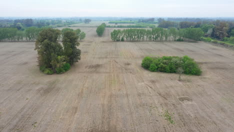 Aerial-view-over-empty-fields,-agricultural-landscape,-prepared-soil-for-sowing-black-soy-seeds-and-planting-wheat,-drone-camera-moving-backwards-slowly