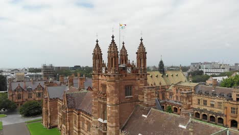 Vista-Panorámica-Del-Campus-De-La-Universidad-De-Sydney,-Australia,-Mostrando-Los-Hermosos-Detalles-Arquitectónicos-De-Su-Edificio-Principal-Y-Una-Bandera-Ondeando-Al-Viento-En-El-Punto-Más-Alto-Del-Techo.