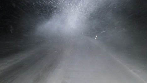 POV-shot-of-two-heavy-logistics-trucks-passing-on-a-dark-icy-snow-covered-highway,-as-the-trucks-pass-the-bright-headlight-beams-obscure-visibility-as-the-vehicle-drives-through-the-snow-trail,-Sweden