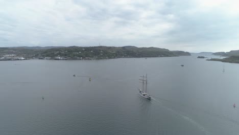 Toma-Aérea-De-Un-Velero-Que-Llega-A-La-Bahía-De-Oban,-Escocia,-En-Un-Día-Nublado