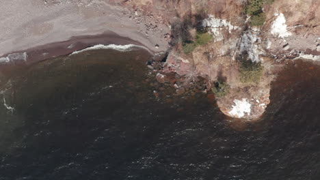 aerial-drone-view-flying-overhead-looking-down-on-and-following-shoreline-of-lake-superior-with-dead-trees-and-small-rock-island-on-sunny-day-in-minnesota-in-winter-off-lake-superior