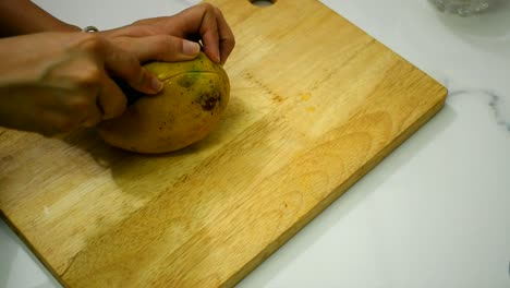 close-of-person-hand-cutting-mango-with-a-knife