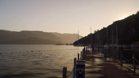 This-editorial-shot-depicts-a-panoramic-view-of-a-person-stretching-on-a-sea-deck-during-hot-summer-surrounded-by-Turkish-mountains