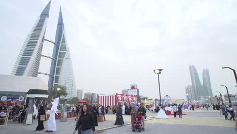 Timelapse-wide-angle-of-the-Bahrain-Food-Festival-at-King-Faisal-Highway-Corniche,-the-Bahrain-World-Trade-Centre-with-its-built-in-wind-turbines-in-the-background-and-light-cloud-above