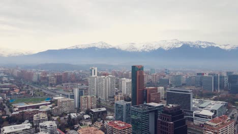 Aerial-orbit-around-main-skyscrapers-of-Santiago-with-the-Andes-mountains-on-the-back,-4K