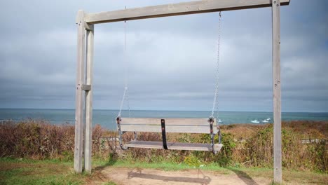 Wide-shot-empty-wooden-swing-bench-overlooking-the-montauk-beach-on-a-partly-cloudy-day