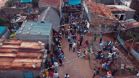 African-rural-village-having-a-wedding-dance-party-in-the-streets-with-flags-blowing-in-the-wind,-shot-from-above-in-the-Comoros,-Africa