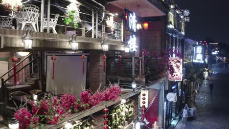 Drohnenflug-über-Einem-Beleuchteten-Chinesischen-Restaurant-Im-Freien-In-Einer-Gasse-Der-Stadt-Guangzhou,-Wo-Menschen-Auf-Der-Straße-Zu-Sehen-Sind