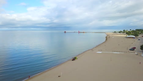 Drone-Aéreo-Disparado-Sobre-Un-Tractor-Que-Conducía-Por-Una-Gran-Playa-De-Arena-Con-Un-Gran-Lago-Y-Un-Faro-Al-Fondo-En-Un-Día-Nublado