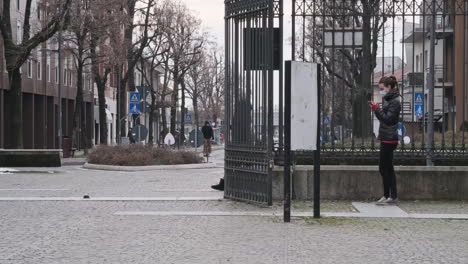 Eine-Junge-Frau-Trägt-Eine-Medizinische-Maske,-Während-Sie-Im-Freien-In-Der-Stadt-Ihr-Smartphone-Benutzt