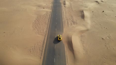 Revealing-aerial-drone-shot-of-a-Chevrolet-Camaro-in-the-middle-of-abandoned-desert-roads-covered-with-sand-in-Dubai,-UAE