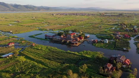 Vuelo-Aéreo-Sobre-Un-Monasterio-De-Madera-Rodeado-De-Jardines-Flotantes,-Myanmar