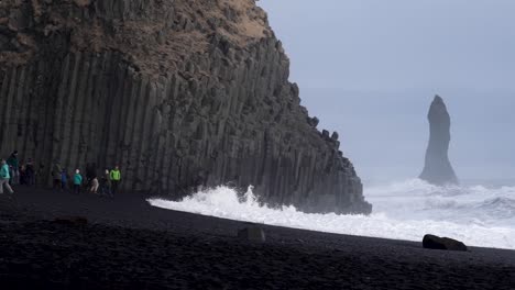 Touristen,-Die-Vor-Den-Wellen-Am-Schwarzen-Sandstrand-Im-Süden-Islands-Fliehen,-Zeitlupen-Handvideo