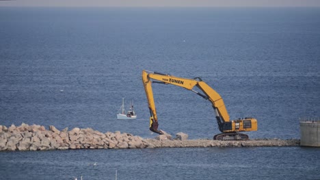 Excavator-moving-stones-on-the-pier-of-hanstholm-harbour,-denmark