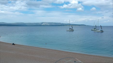 Un-Pequeño-Barco-Lleno-De-Gente-Detrás-De-Un-Velero-En-La-Playa-De-Zlatni-Rat,-Croacia