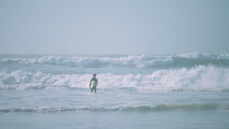 Gimbal-shot-of-surfer-entering-sea-with-surfboard-under-arm