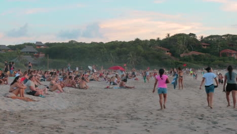 Gran-Multitud-De-Jóvenes-Viajeros-Sentados-Y-Relajándose-En-La-Arena-Junto-A-Una-Playa-Y-Contemplando-La-Puesta-De-Sol-En-México---Cámara-Lenta