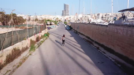 Slow-mo-active-track-drone-shot-of-a-young,-athletic,-woman-inline-skating-on-the-streets-from-the-back-in-the-middle-of-parking-cars,-waving-her-arms-up-as-she-is-gliding-through-the-windy-breeze