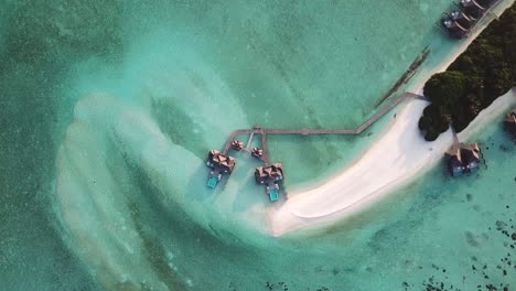 Aéreo,-Destornillador,-Disparo-De-Drone,-Elevándose-Sobre-Una-Playa-De-Arena-Blanca-Y-Bungalows-Sobre-El-Agua,-En-Una-Laguna-Turquesa,-En-Un-Día-Soleado,-En-La-Isla-Conrad-Rangoli,-En-Maldivas