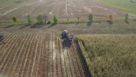 Tractor-with-chaser-bin-turning-left-on-field,-after-harvesting-maize,-aerial