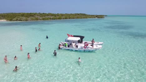 Vista-Aérea-La-Gente-Disfruta-De-Una-Fiesta-En-La-Playa-Dentro-Del-Agua-De-Mar-Con-Barcos-Amarrados,-Los-Roques