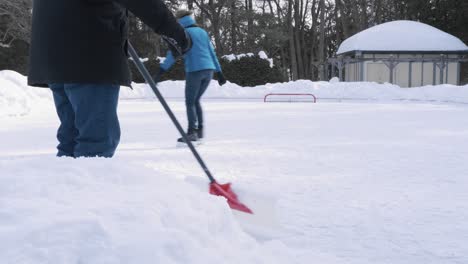 Caucasian-family-skating-at-an-outdoor-skating-rink,-dad-clears-the-snow-with-a-"Hosers"-shovel