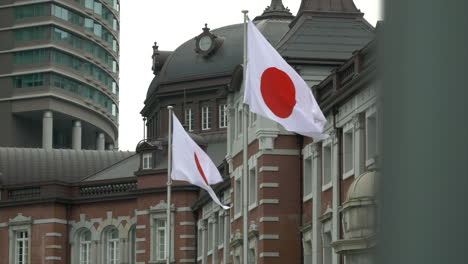 Twin-Japanese-flags-in-front-of-the-main-train-station-Tokyo,-Japan,-Slow-motion-reveal-left-to-right