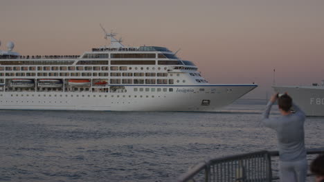 Passenger-Cruise-Ship-Insignia-Seen-Reversing-On-The-River-Hudson-Viewed-From-Pier-With-Person-Taking-Photo-During-Evening-Sunset