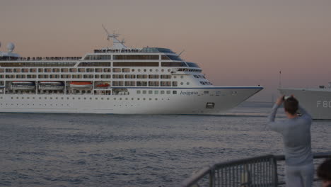 Se-Ve-La-Insignia-De-Un-Crucero-De-Pasajeros-Dando-Marcha-Atrás-En-El-Río-Hudson-Vista-Desde-El-Muelle-Con-Una-Persona-Tomando-Fotos-Durante-El-Atardecer