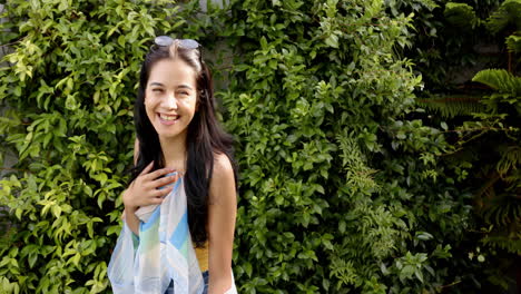 A-young-biracial-woman-smiles-brightly,-surrounded-by-lush-greenery,-copy-space
