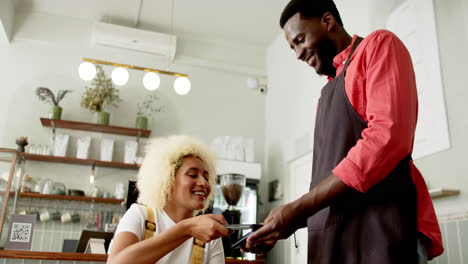 A-young-biracial-woman-is-paying-with-a-smartphone-to-an-African-American-worker-in-a-cafe