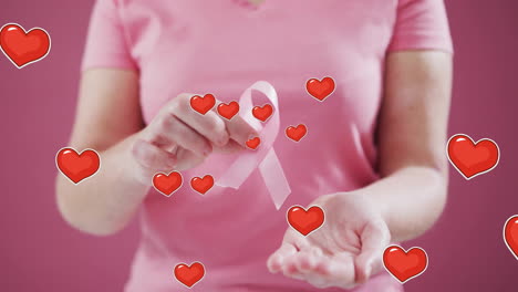 Animation-of-hearts-over-caucasian-woman-holding-pink-ribbon