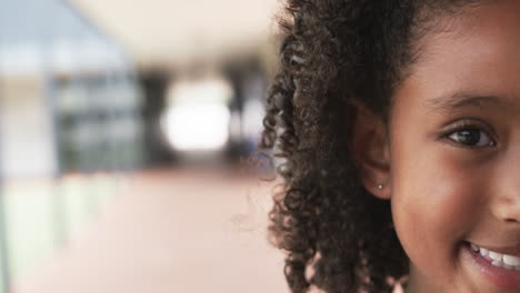 Close-up-of-a-smiling-biracial-girl-with-curly-hair,-with-copy-space,-in-school