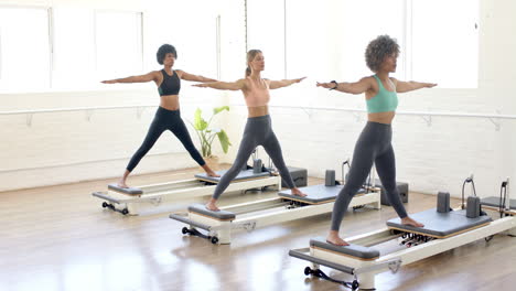 Three-women-are-practicing-yoga-on-pilates-reformers-in-bright-studio