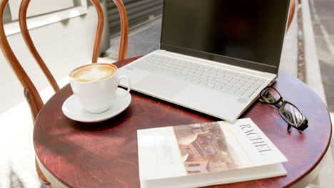 Ein-Laptop,-Eine-Tasse-Kaffee,-Eine-Brille-Und-Eine-Zeitschrift-Liegen-Auf-Einem-Cafétisch