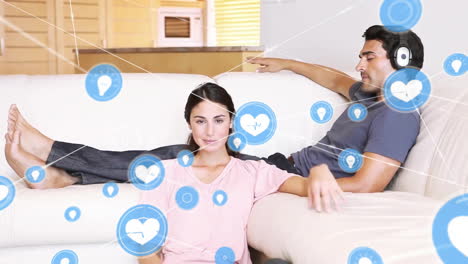 Animation-of-network-of-connections-with-icons-over-caucasian-couple-watching-tv