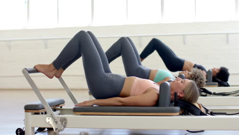 Three-women-are-exercising-on-pilates-reformer-machines-in-bright-studio